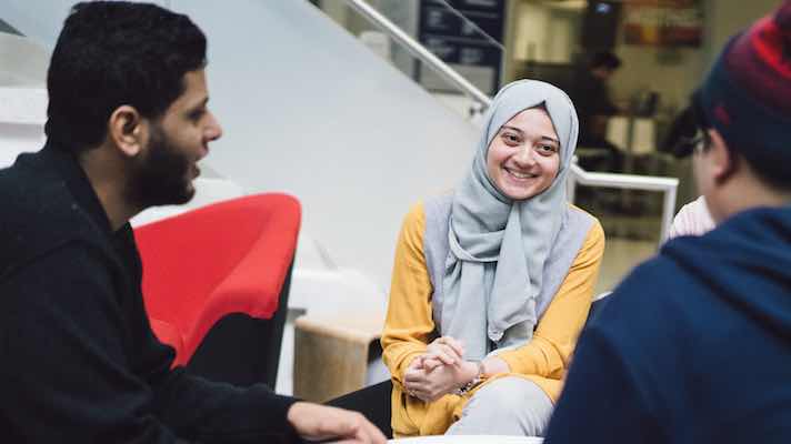 Students of a diverse background gathered around a table and engaged in a discussion 