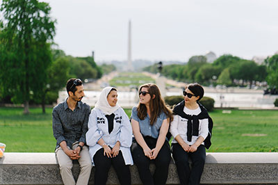 Four ELC students seated near US capitol with Washington monument in background